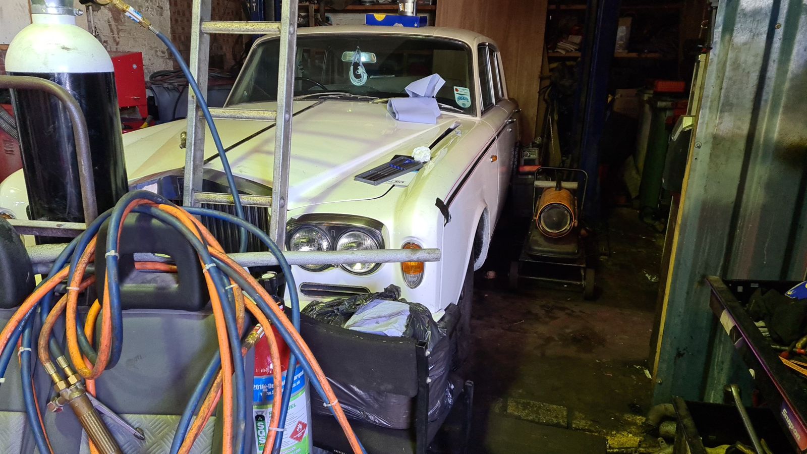 A white classic Rolls-Royce in the workshop behind gas welding hoses